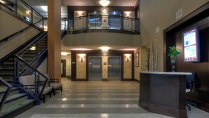 A lobby with a staircase, elevators, a reception desk, and a plant.