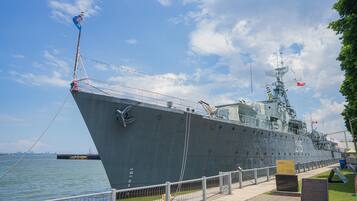 A large naval ship docked at a port with a clear sky and a grassy area in the foreground.