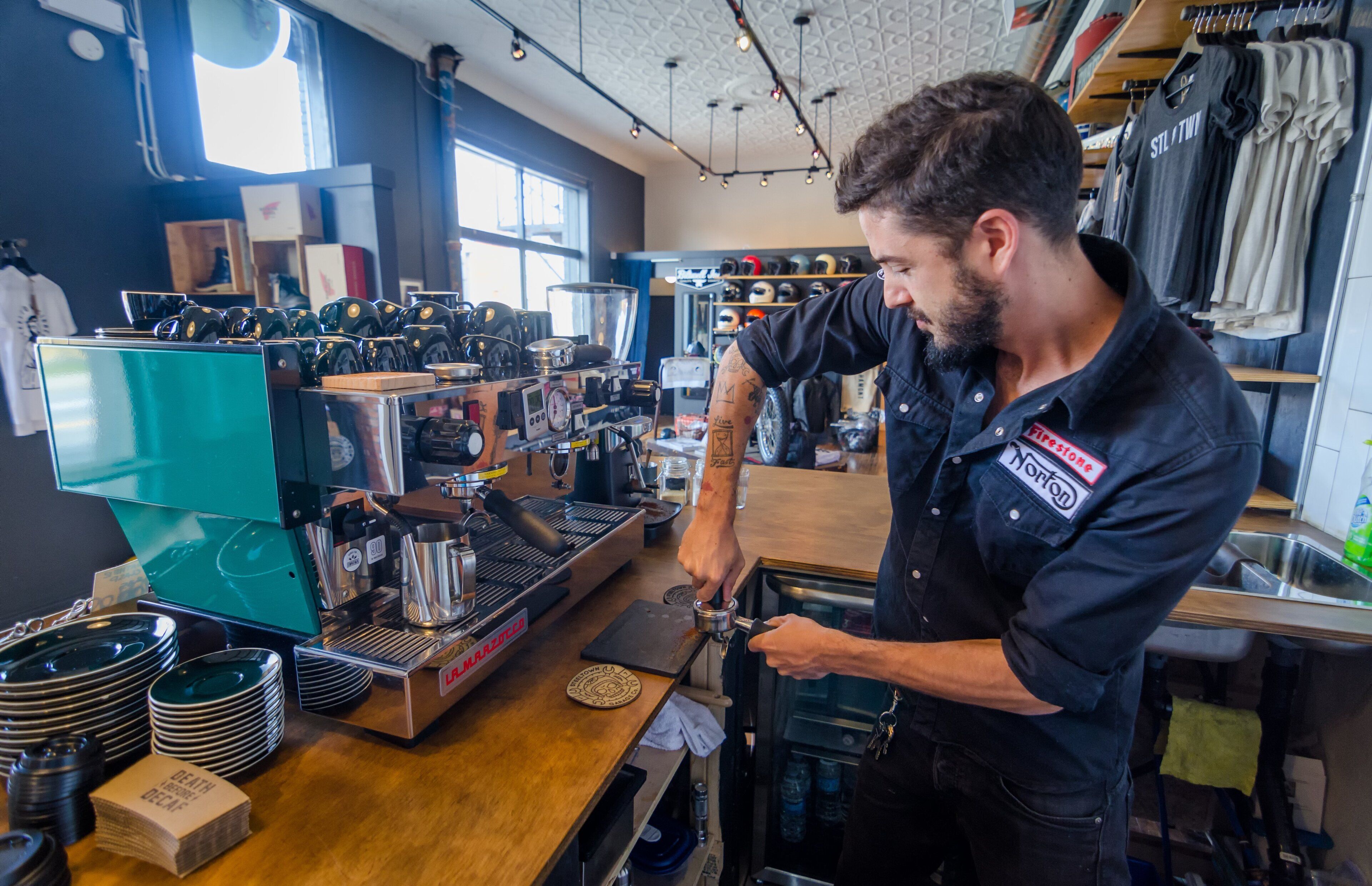 A person operating a coffee machine in a cafe with various coffee-making equipment and a window in the background.