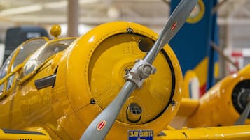 Un avión amarillo con hélice, un letrero que dice "DISFRUTA LAS EXHIBICIONES Por favor, NO TOCAR" y un fondo azul y amarillo.