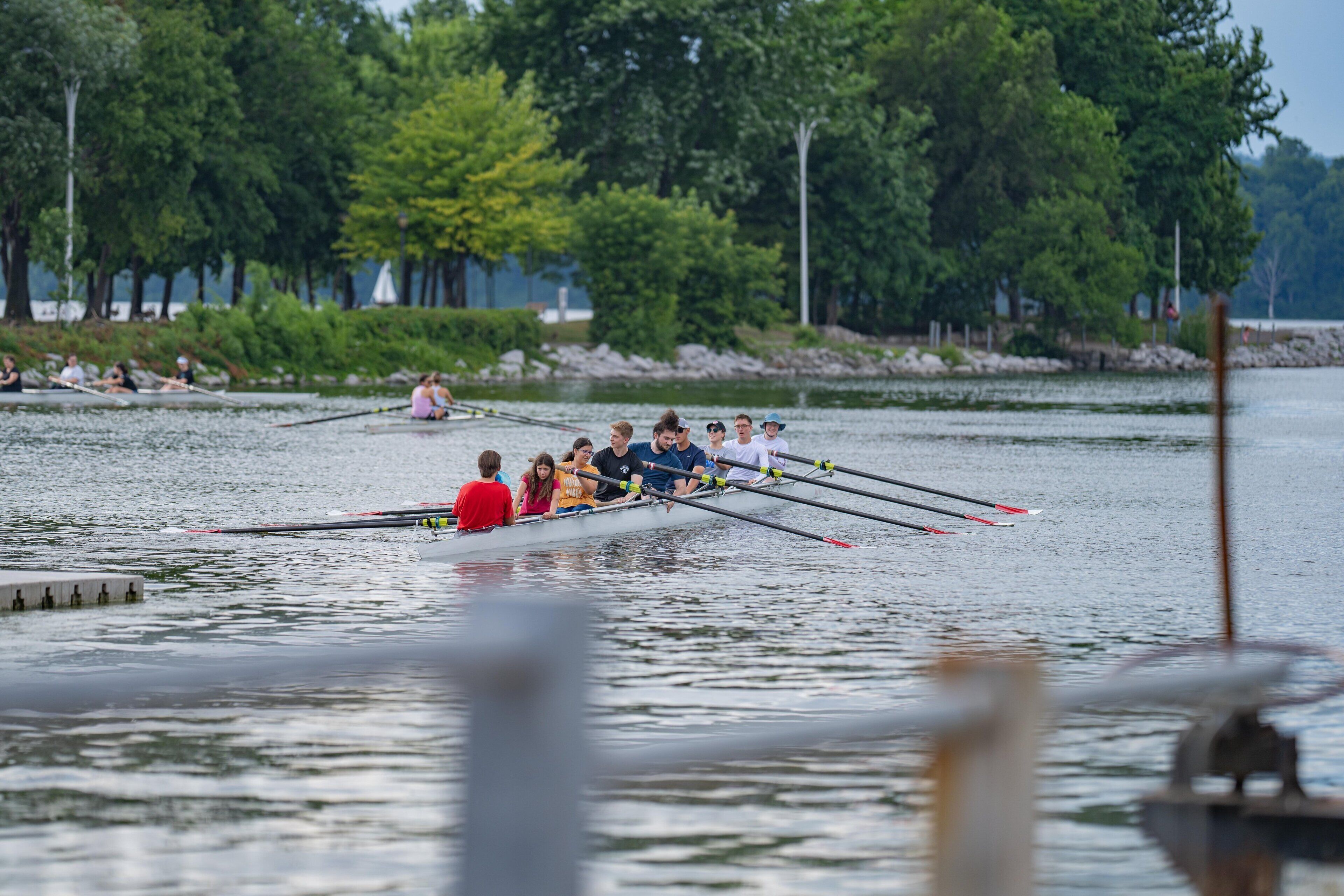 A rowing team in a boat on a calm lake with trees in the background.