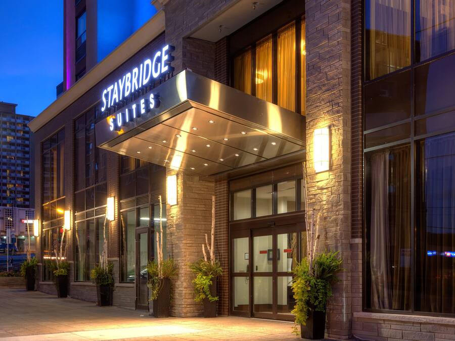 Een Staybridge hotel met een gevel van baksteen, een grote glazen ingang en buitenverlichting.