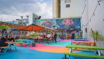 An outdoor seating area with colorful tables and benches, a mural on the wall, and a building in the background.