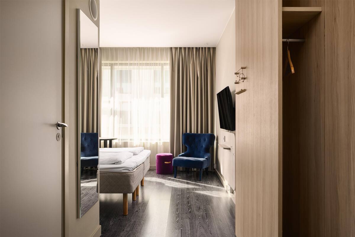Habitación de hotel con cama, una silla, televisor y armario.