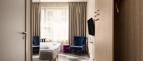 Habitación de hotel con cama, una silla, televisor y armario.
