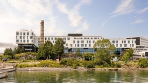 A modern building with a unique cylindrical tower, a waterfront view, and a sign indicating no parking. - Scandic Fornebu (Bærum)