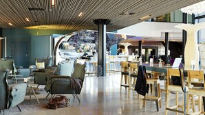 A modern lounge area with seating, a bar, and a large window overlooking the interior. - Scandic Fornebu (Bærum)