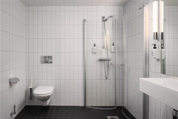 A modern bathroom with a toilet, a glass-enclosed shower, and a white sink. - Scandic Fornebu (Bærum)