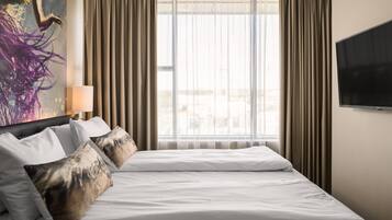 Habitación de hotel con una cama grande, un televisor de pantalla plana, una ventana con cortinas y un cuadro en la pared.