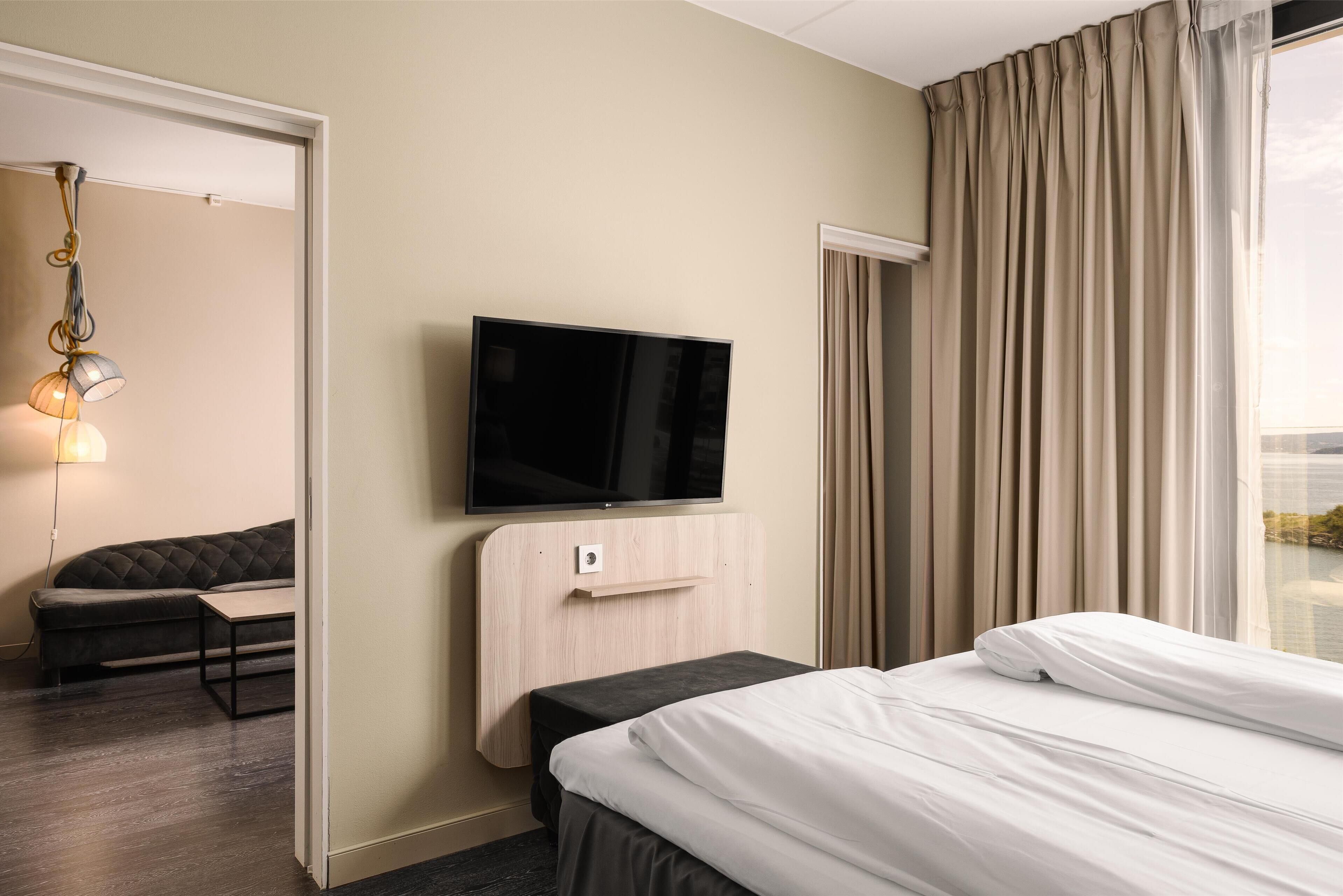 Una habitación de hotel con una cama, un televisor en la pared, un sofá y una ventana con cortinas.