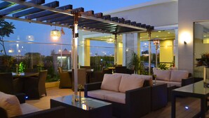 An outdoor seating area with wicker furniture, glass tables, and hanging lights.