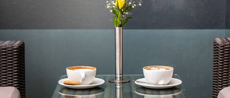 Una mesa con dos tazas blancas de café y un florero con una flor amarilla.