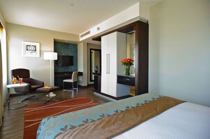 Una habitación de hotel con cama, escritorio, silla, televisor y minibar.