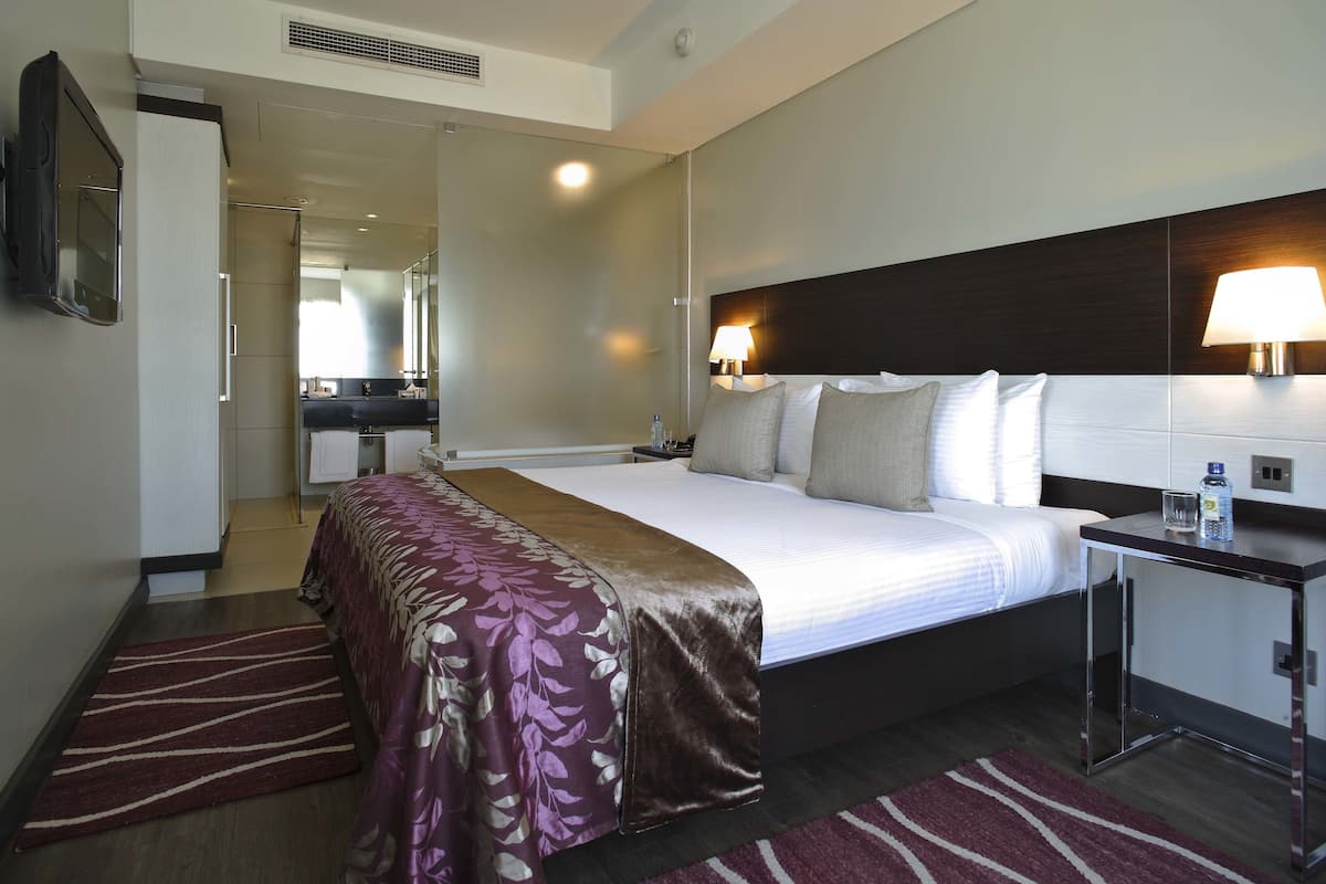 A hotel room with a large bed, a bedside table, a mirror, and a bathroom visible through an open door.