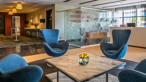 Un'accogliente hall moderna con sedie blu, un tavolo in marmo con un vaso di fiori e una reception con divisorio in vetro.