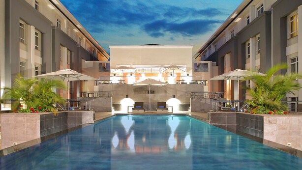 Una piscina con lettini e ombrelloni, circondata da edifici dallo stile architettonico moderno.