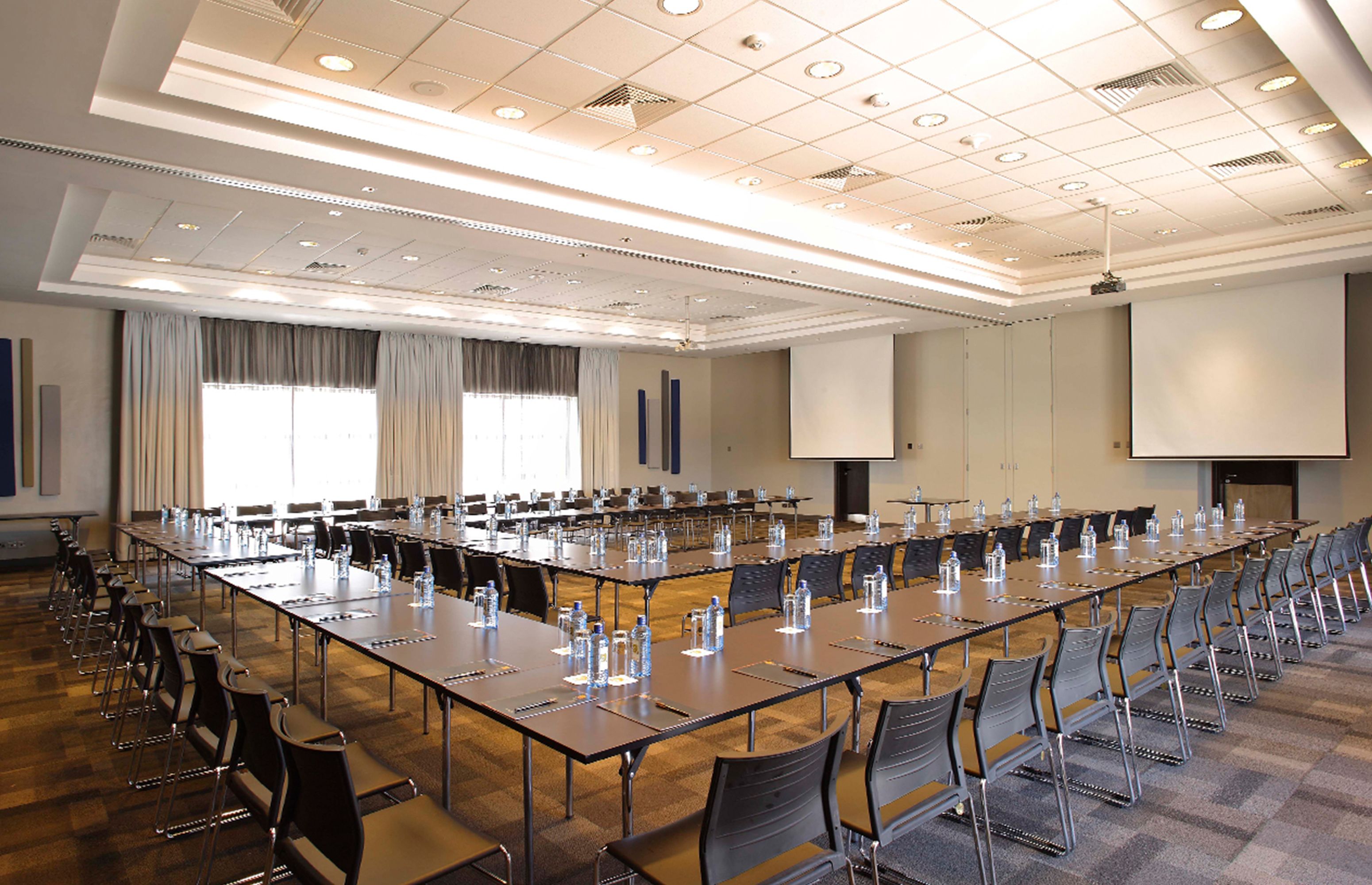 Un salón de conferencias con largas mesas, sillas y una pantalla para proyector.