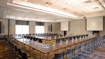 A conference room with long tables, chairs, and a projector screen.