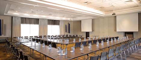 Un salón de conferencias con largas mesas, sillas y una pantalla para proyector.