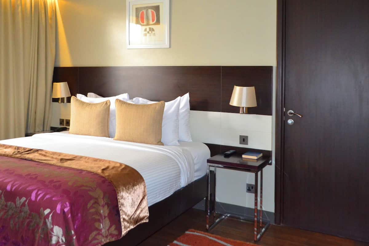 A hotel room with a large bed, two bedside lamps, a nightstand, a framed picture on the wall, and a door.