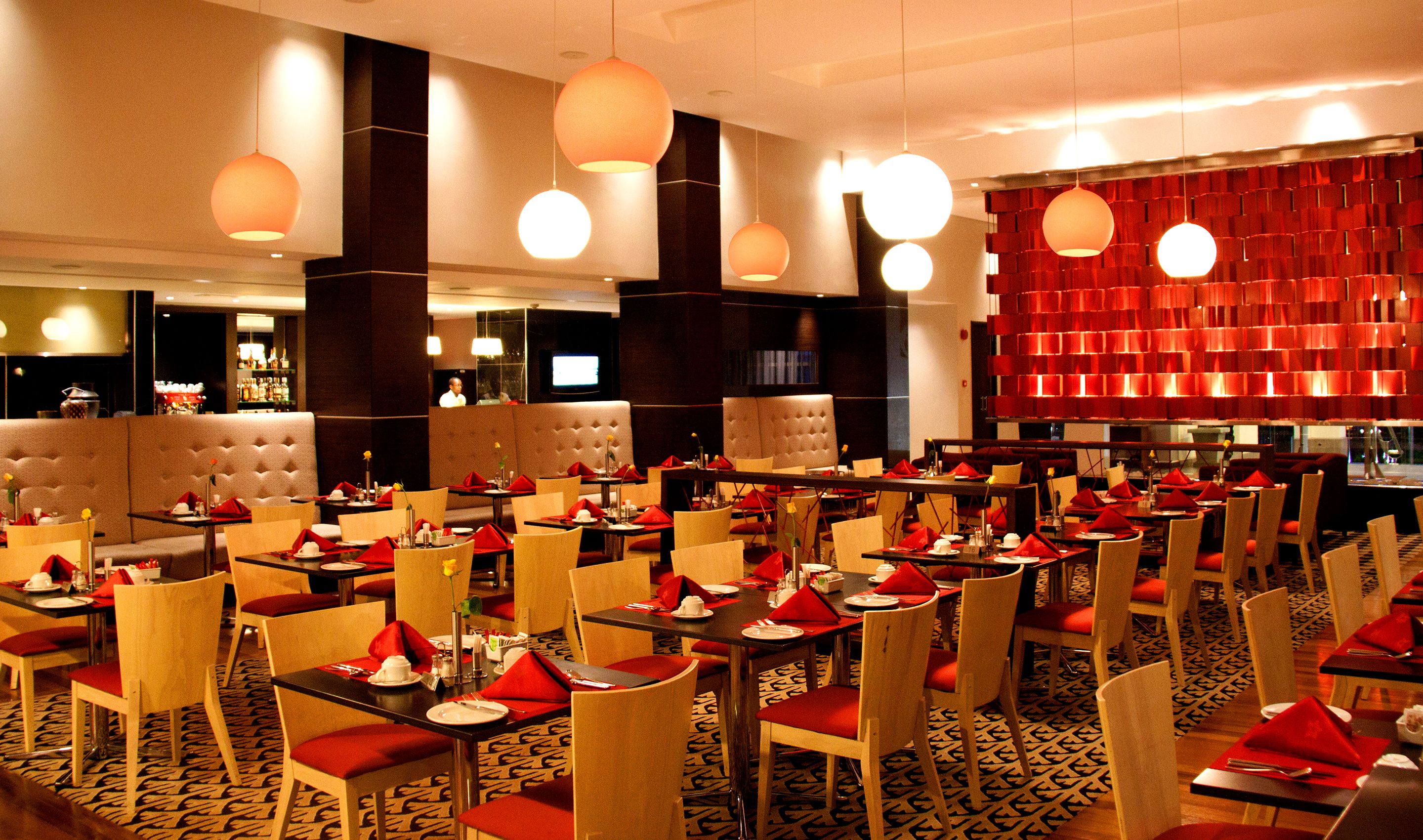 A restaurant with multiple tables and chairs, a bar area, and a red decorative wall.
