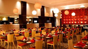 A restaurant with multiple tables and chairs, a bar area, and a red decorative wall.