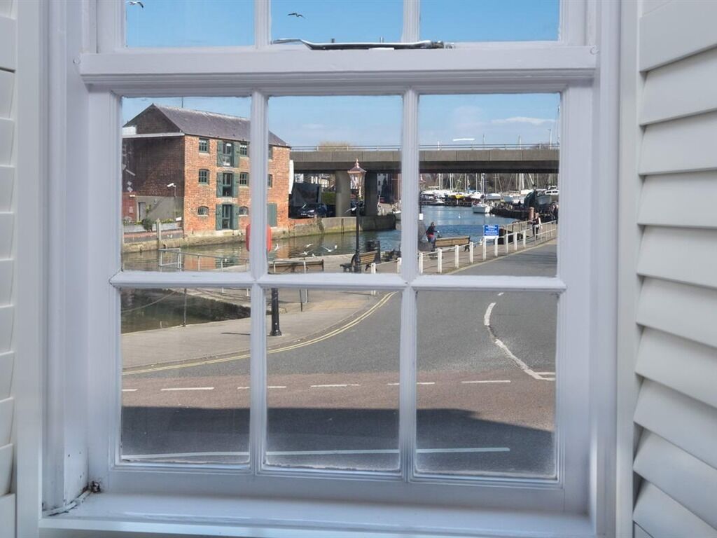 A view through a window of a street with a bridge, buildings, and a canal with boats.