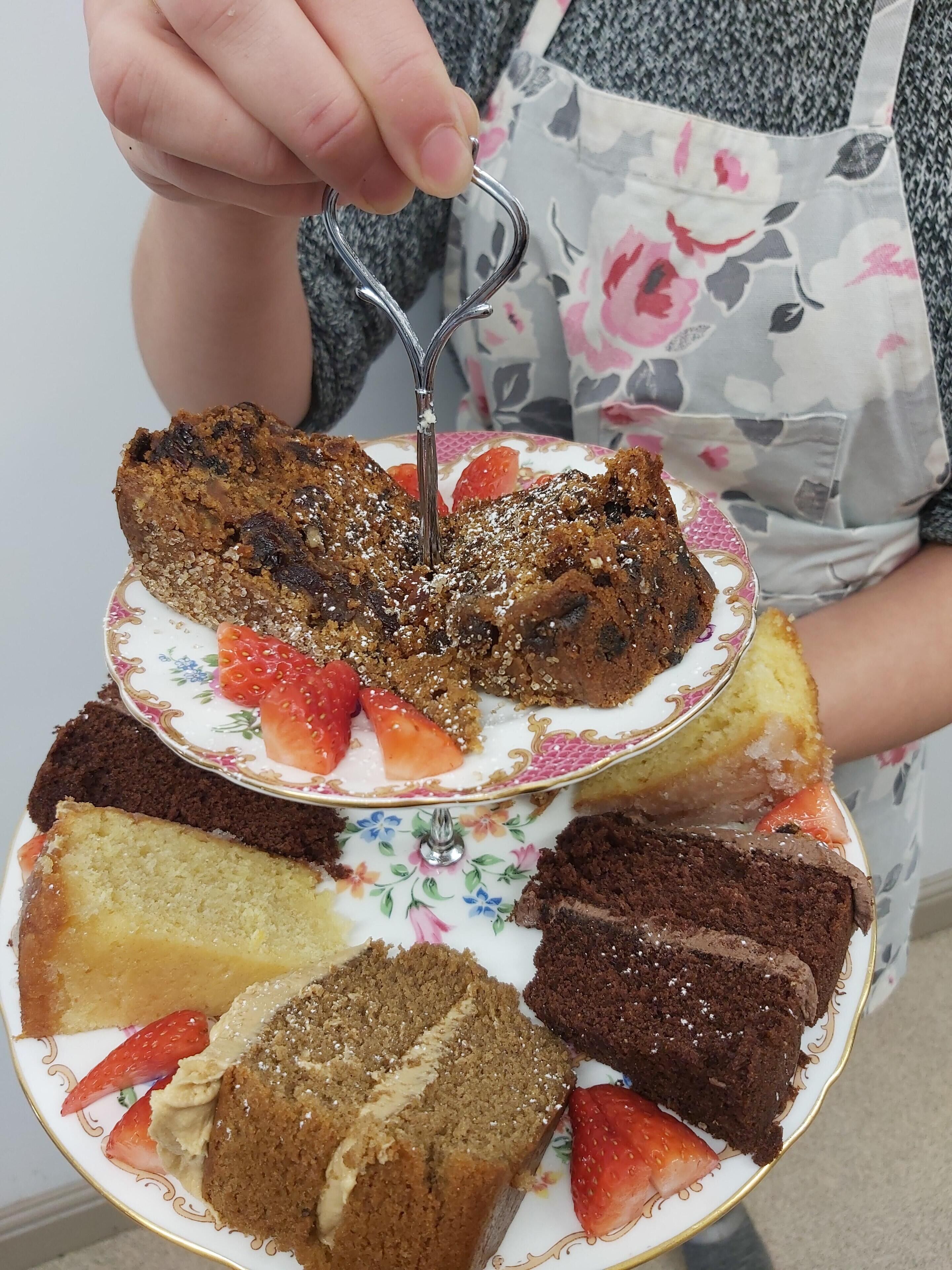 Un pastel de varias capas con fresas y un adorno metálico decorativo, sostenido por una persona con delantal.
