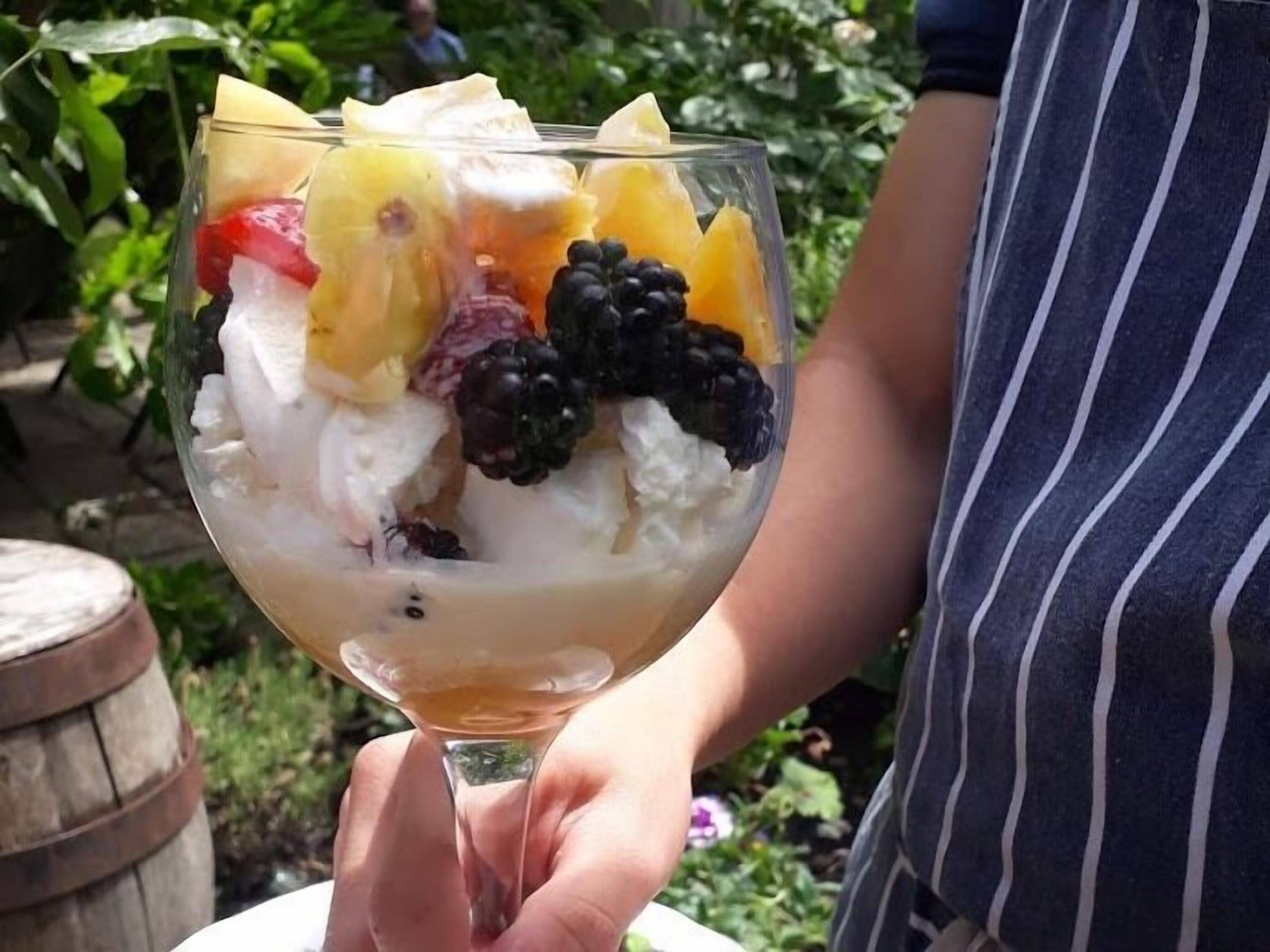 A person holding a dessert glass with various fruits and a scoop of ice cream.