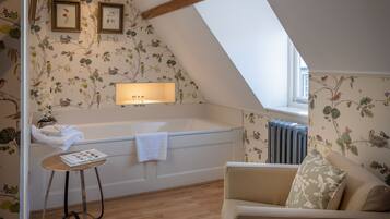 A room with a sloped ceiling, a bathtub, a radiator, a sofa, and a small table with a magazine.