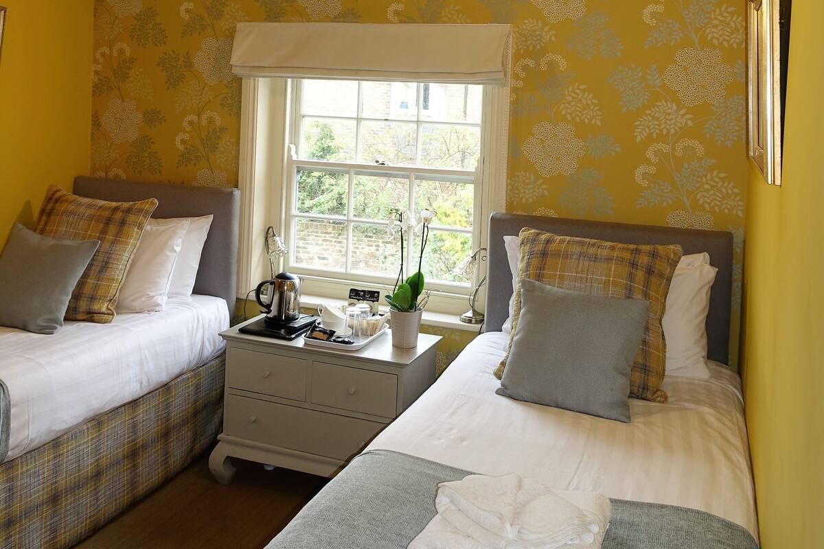 A room with two beds, a nightstand, and a window with a view of greenery.