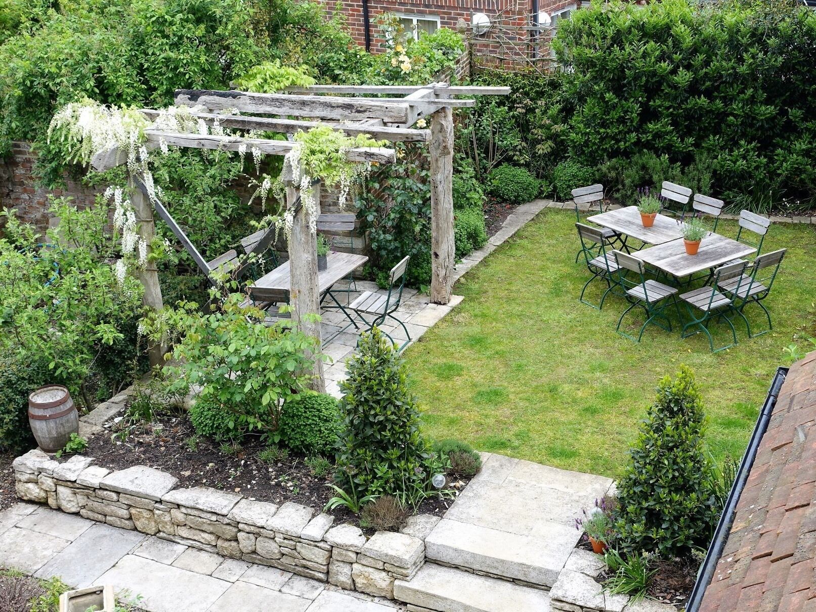 En gårdhave med pergola, sten trapper og et bord med stole.