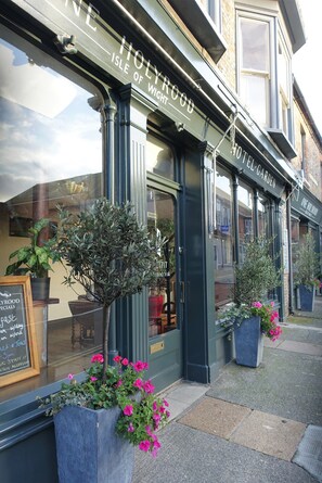 The exterior of The Holyrood Hotel, Isle of Wight, with a signboard, potted plants, and a window displaying a menu. - One Holyrood Hotel (Newport)