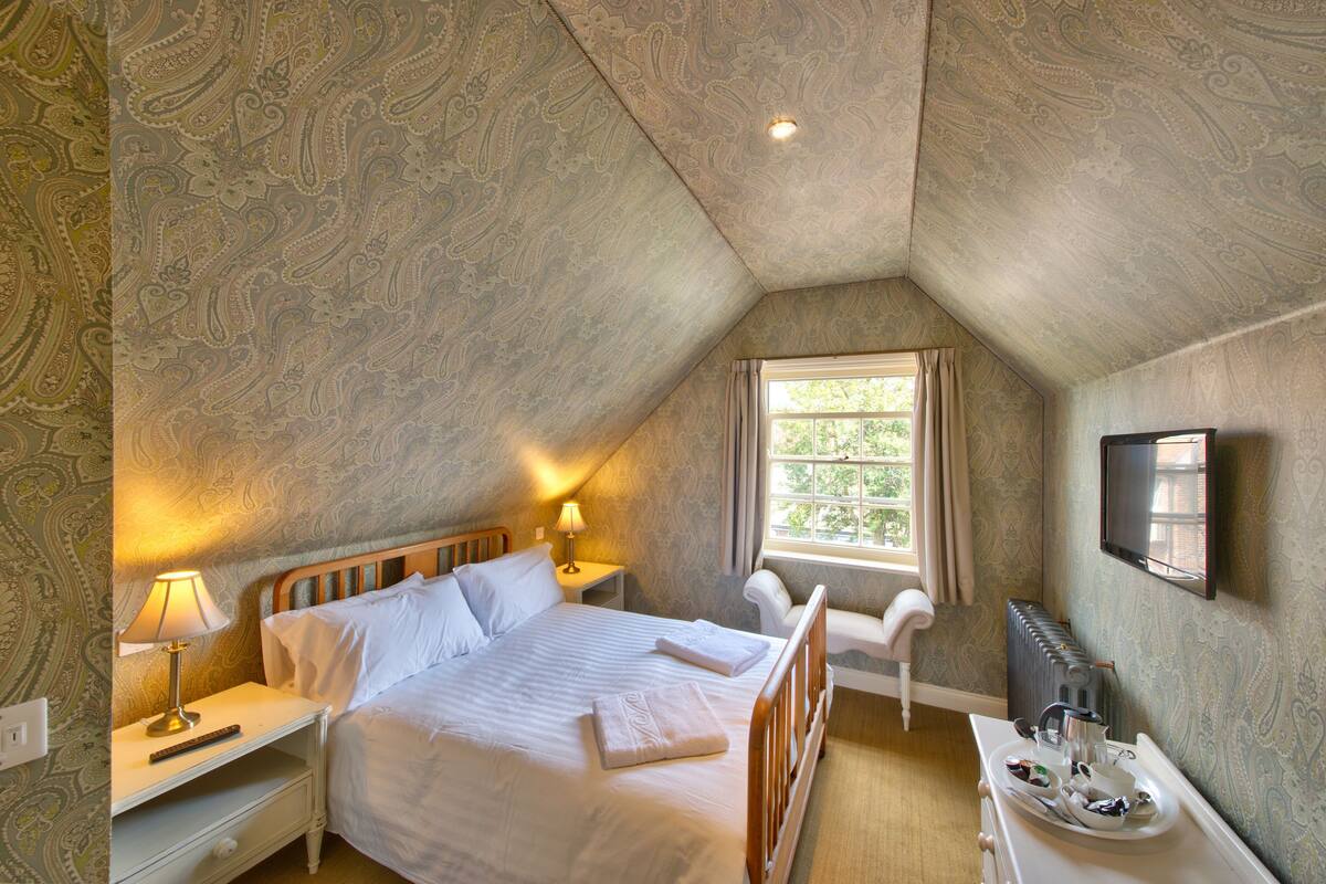A bedroom with a bed, bedside tables, a TV, and a window.