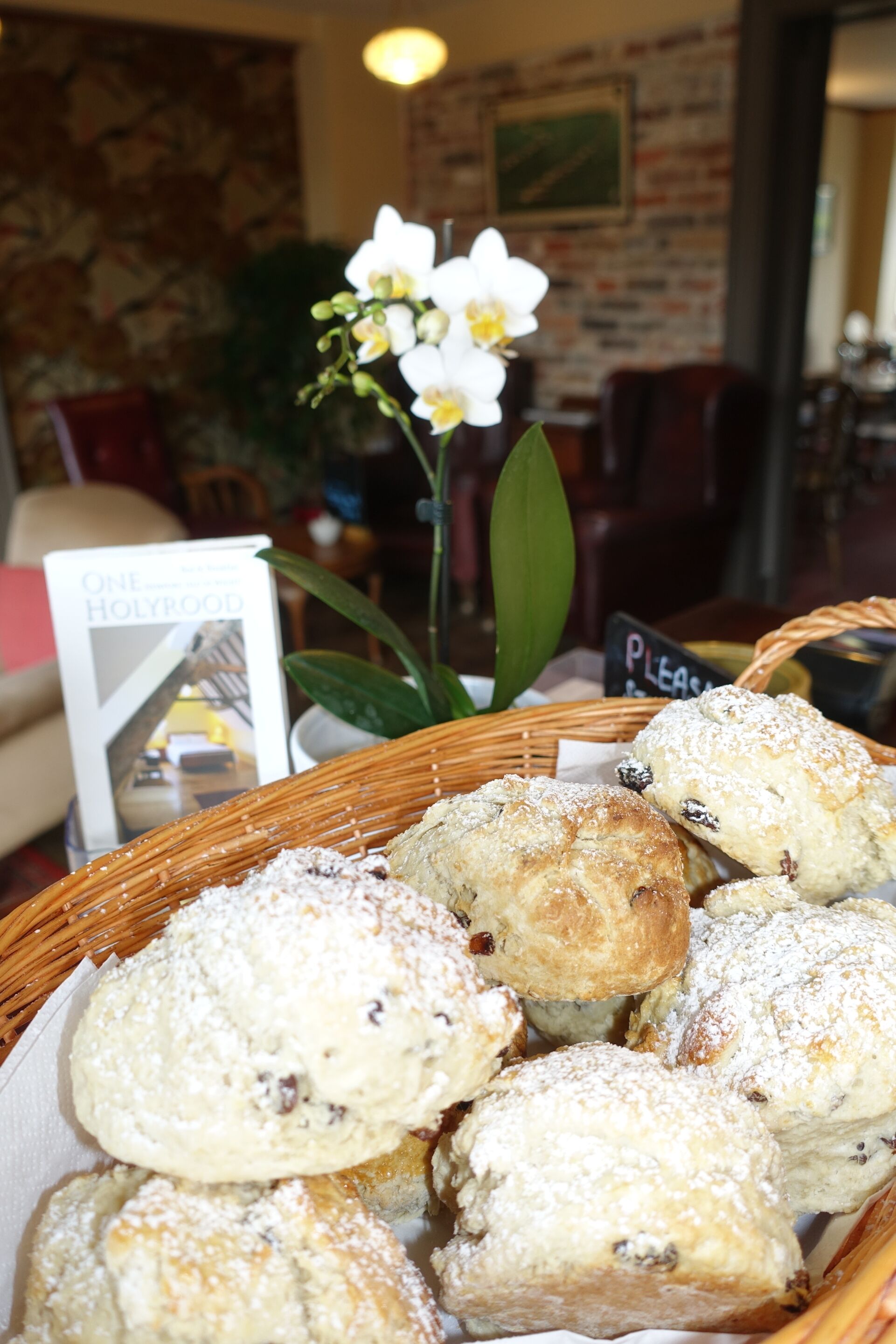 A basket of pastries on a table with a sign that says "Please."