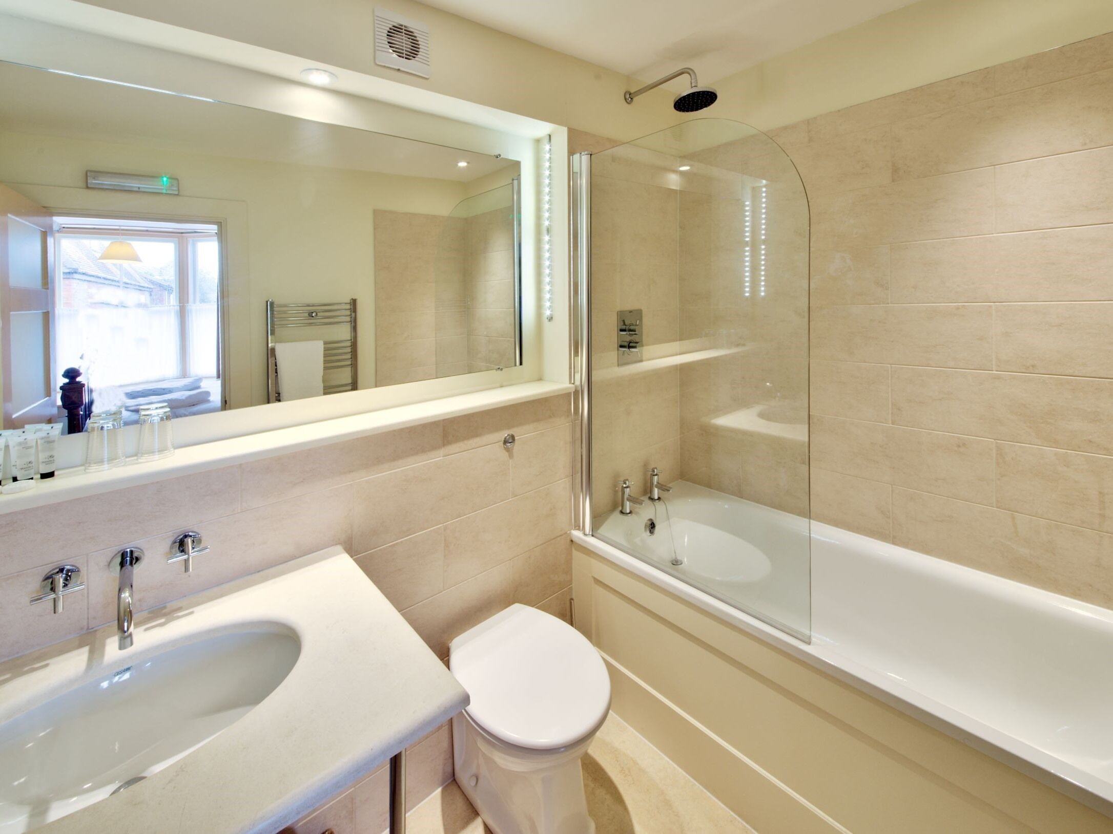 A modern bathroom with a large mirror, a bathtub, a toilet, and a sink.