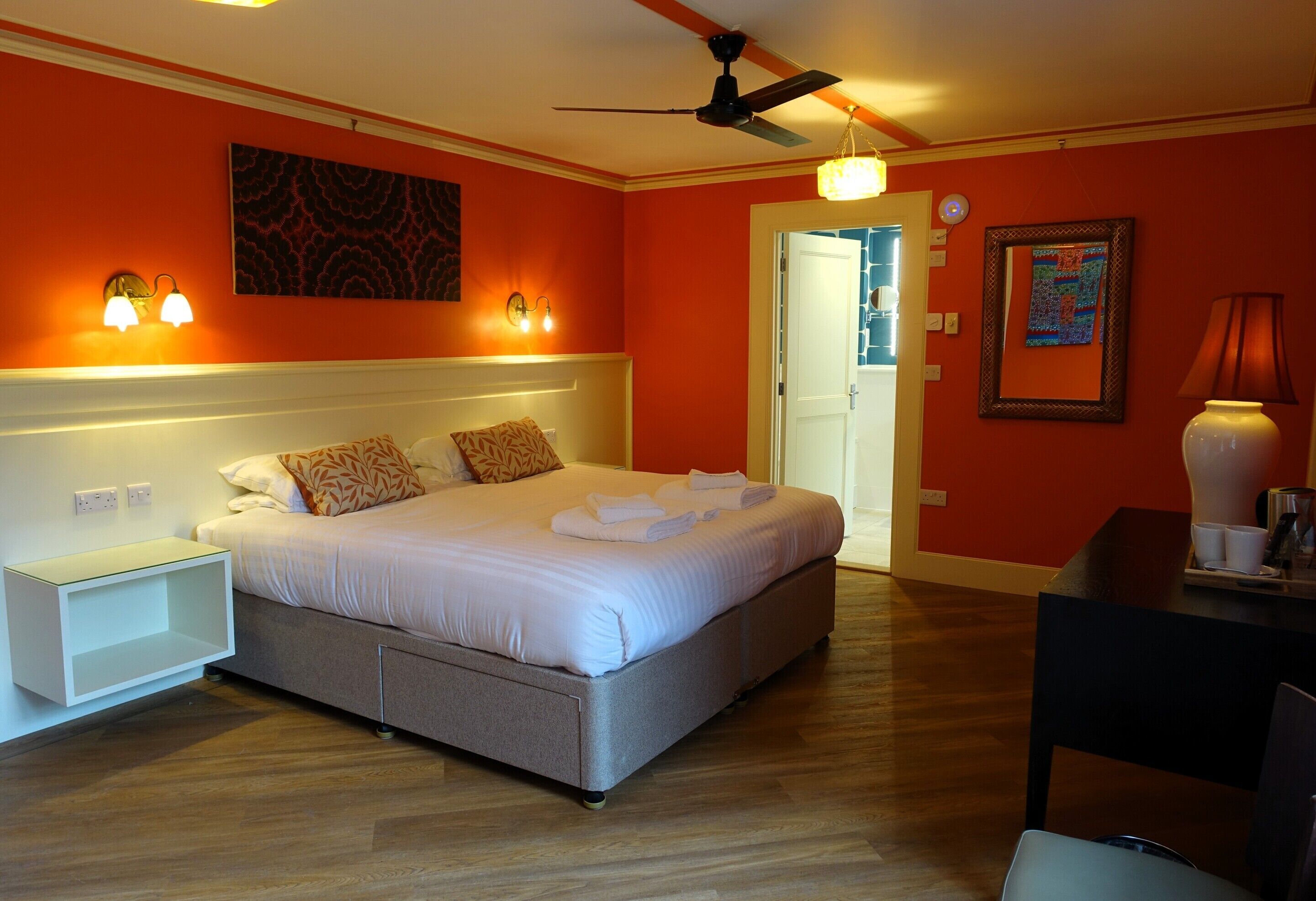 A bedroom with a bed, bedside tables, a ceiling fan, and a door leading to another room.