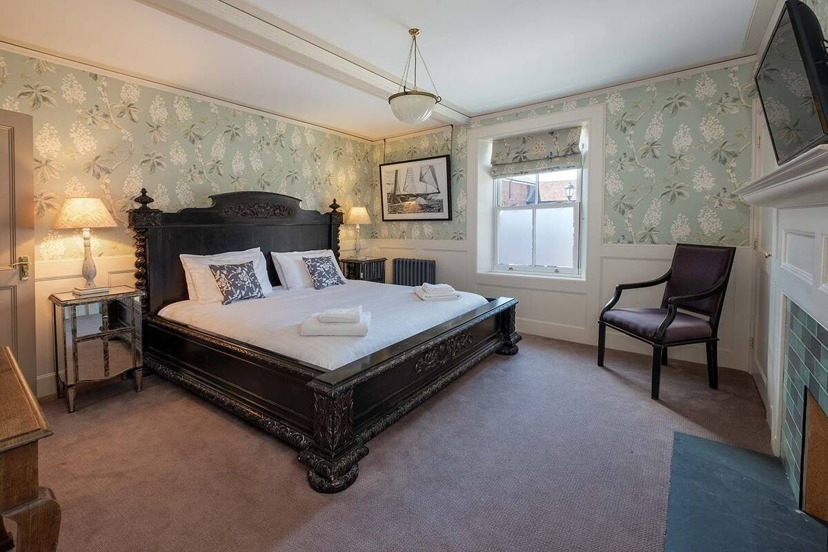 A bedroom with a large bed, two bedside tables with lamps, a chair, a window with a view, and a fireplace.