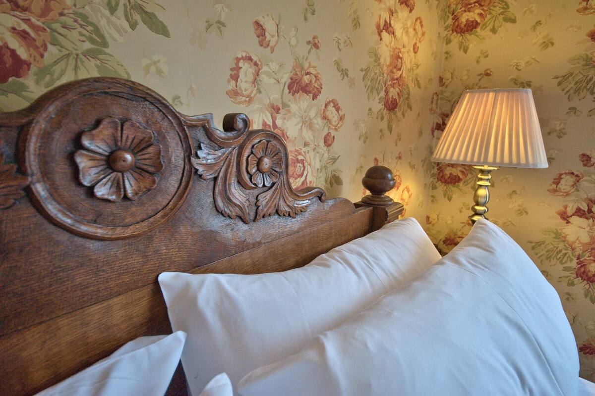 A wooden headboard with floral carvings, a white pillow, and a bedside lamp.