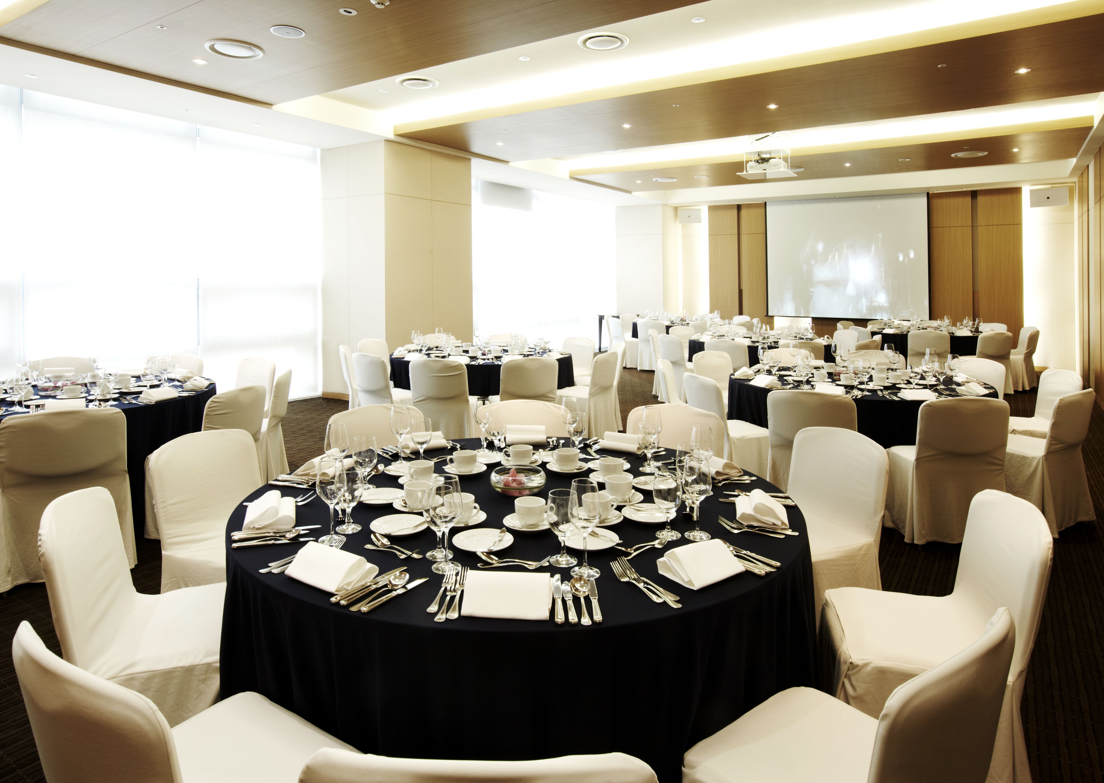 Un salón de conferencias con varias mesas redondas dispuestas para comer, cada una rodeada de sillas blancas.