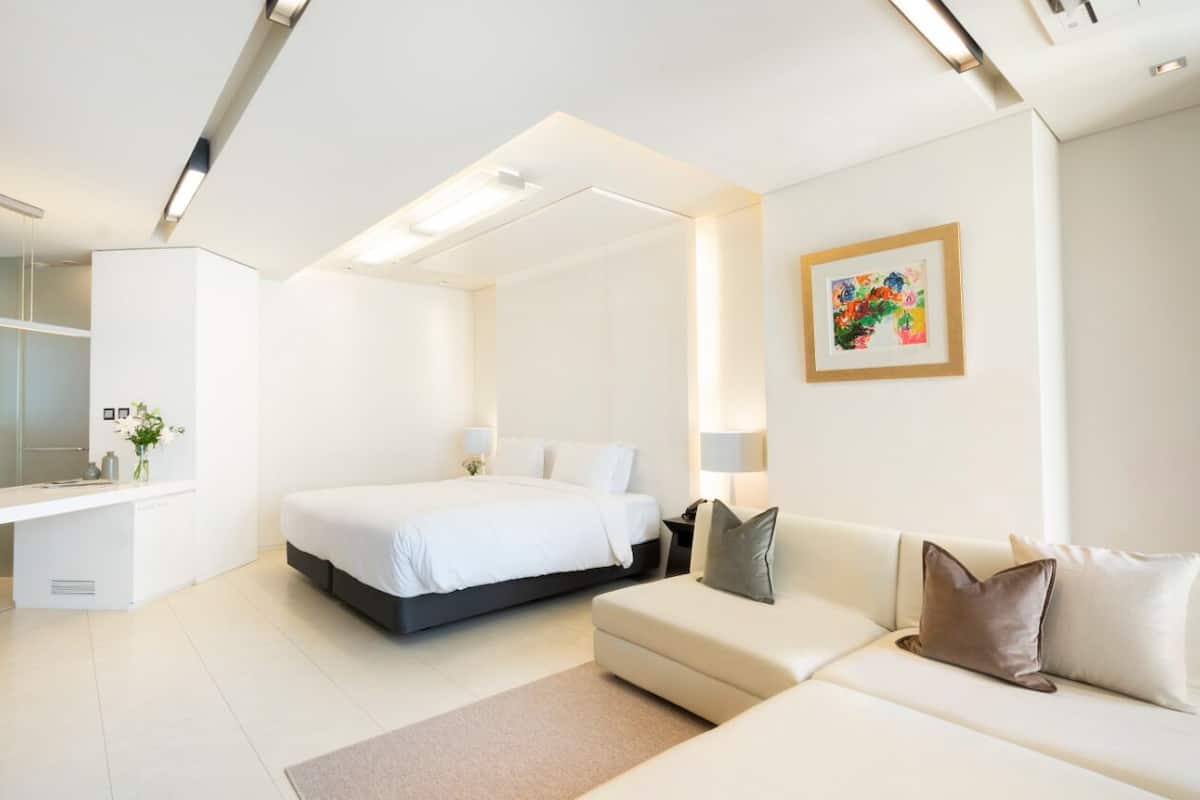 A modern hotel room with a bed, a sofa, a desk, and a bathroom.