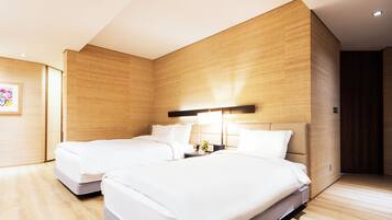 A hotel room with two beds, wooden walls, a nightstand with a lamp, and a small table with a vase of flowers.