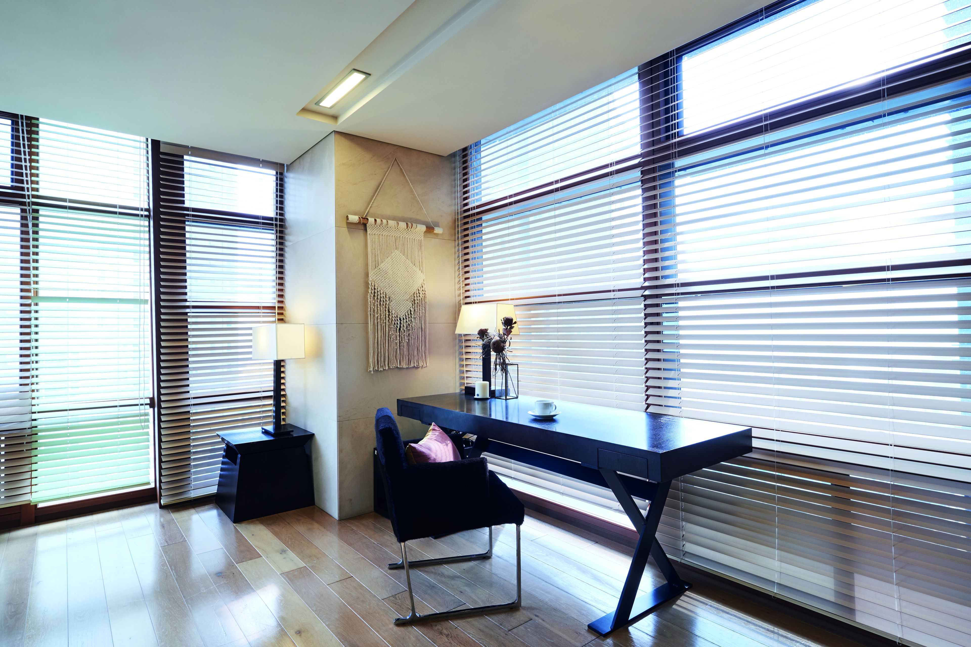Habitación moderna con escritorio, silla y ventanas grandes con persianas.
