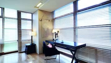 Habitación moderna con escritorio, silla y ventanas grandes con persianas.