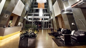 A modern lobby with a high ceiling, geometric wall patterns, and a central chandelier.