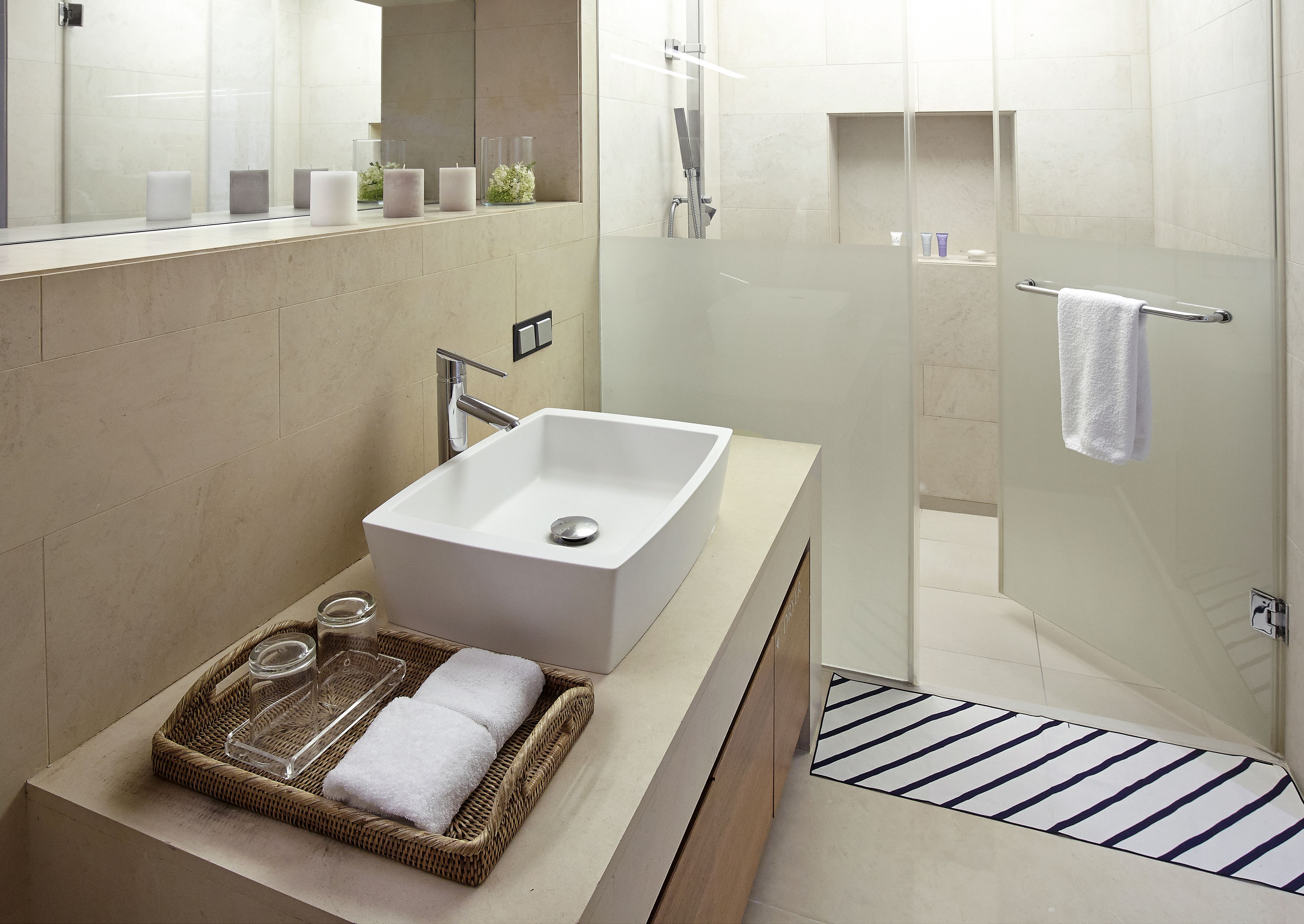 A modern bathroom with a large rectangular sink, a glass shower enclosure, and a striped floor mat.