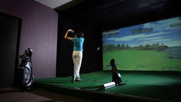 Una persona practica un swing de golf en un simulador con una pantalla grande que muestra un campo de golf.