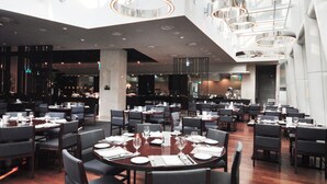 A spacious dining area with high ceilings, modern lighting fixtures, and a view of the sky through large windows.