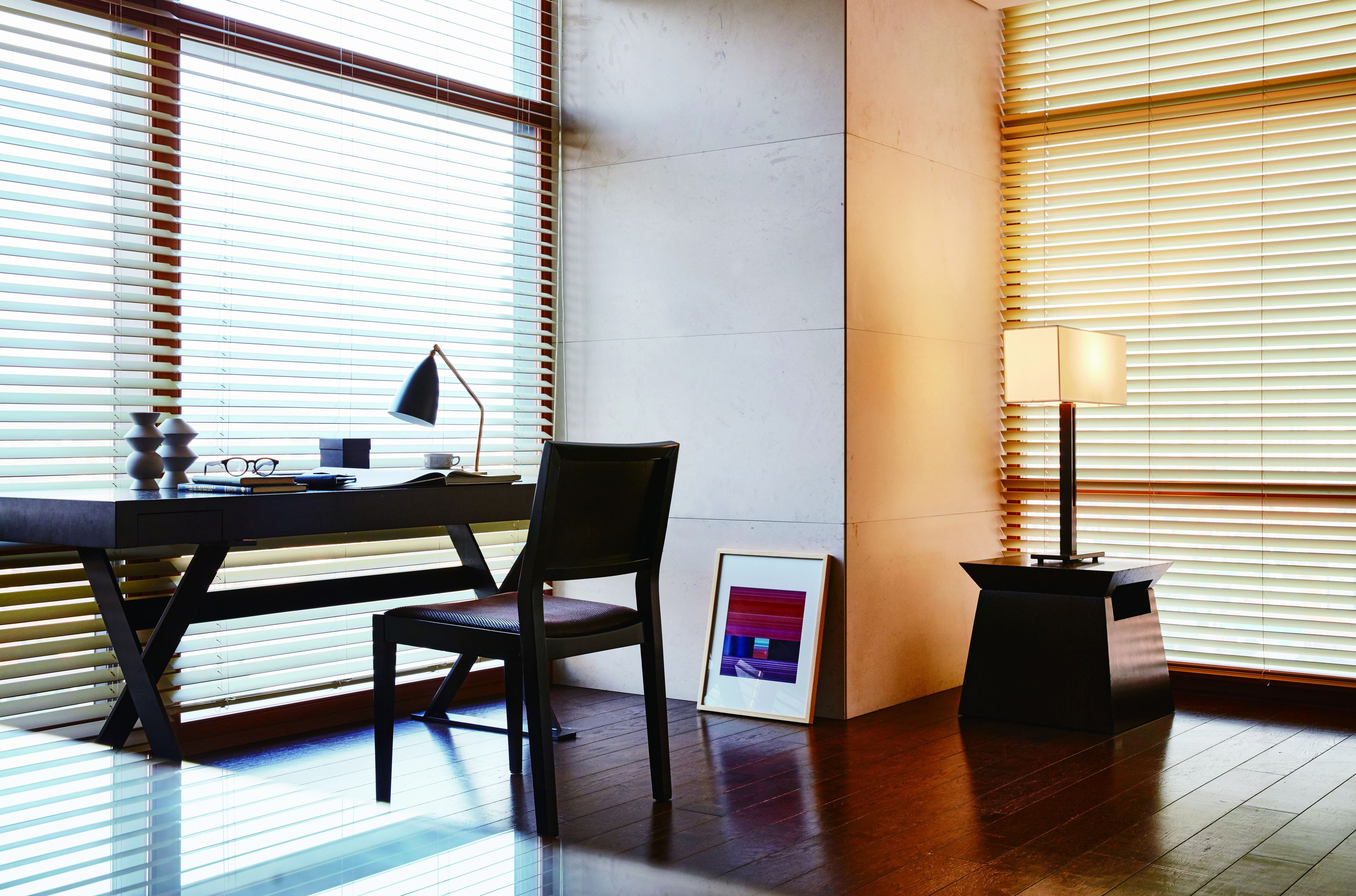 A modern office space with a desk, chair, framed picture, and a standing lamp.
