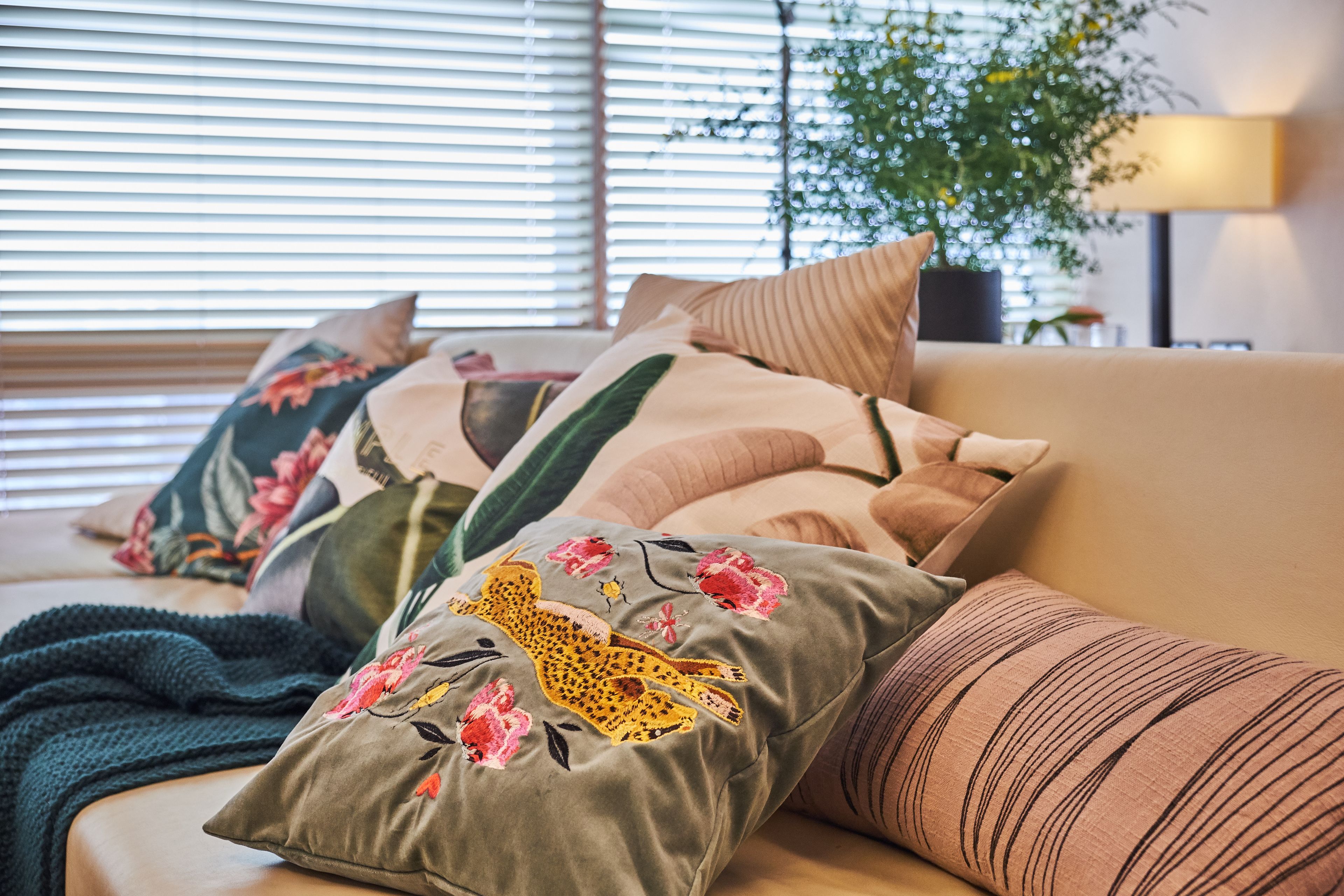 Ein Bett mit blumigen und gestreiften Kissen, einer grünen Decke und einer Pflanze im Hintergrund.